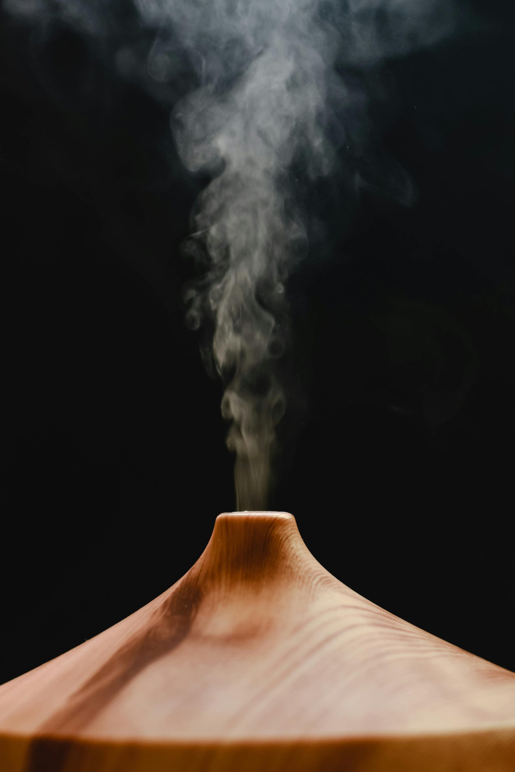 Elegant wooden diffuser releasing smoke on a black background, ideal for aromatherapy themes.